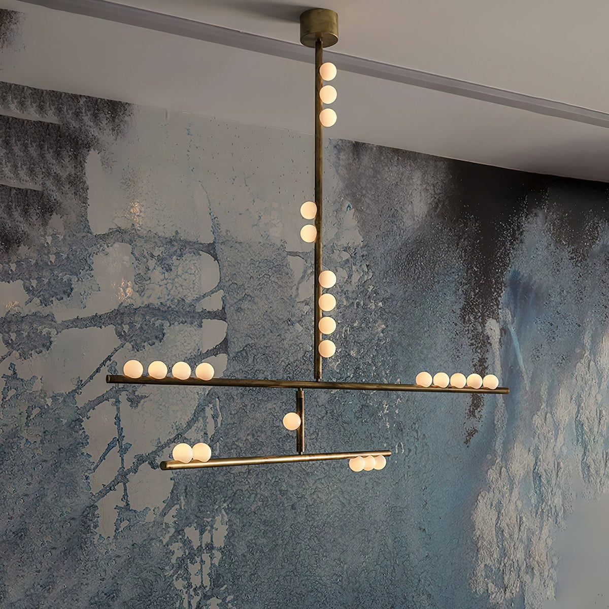 Close view of the brass rod and lit white orbs on this Clérachic pendant, against a blue and grey textured wall.