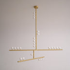 A brass Clérachic pendant with a round ceiling plate and white orbs along its bars, unlit on a pale grey backdrop.
