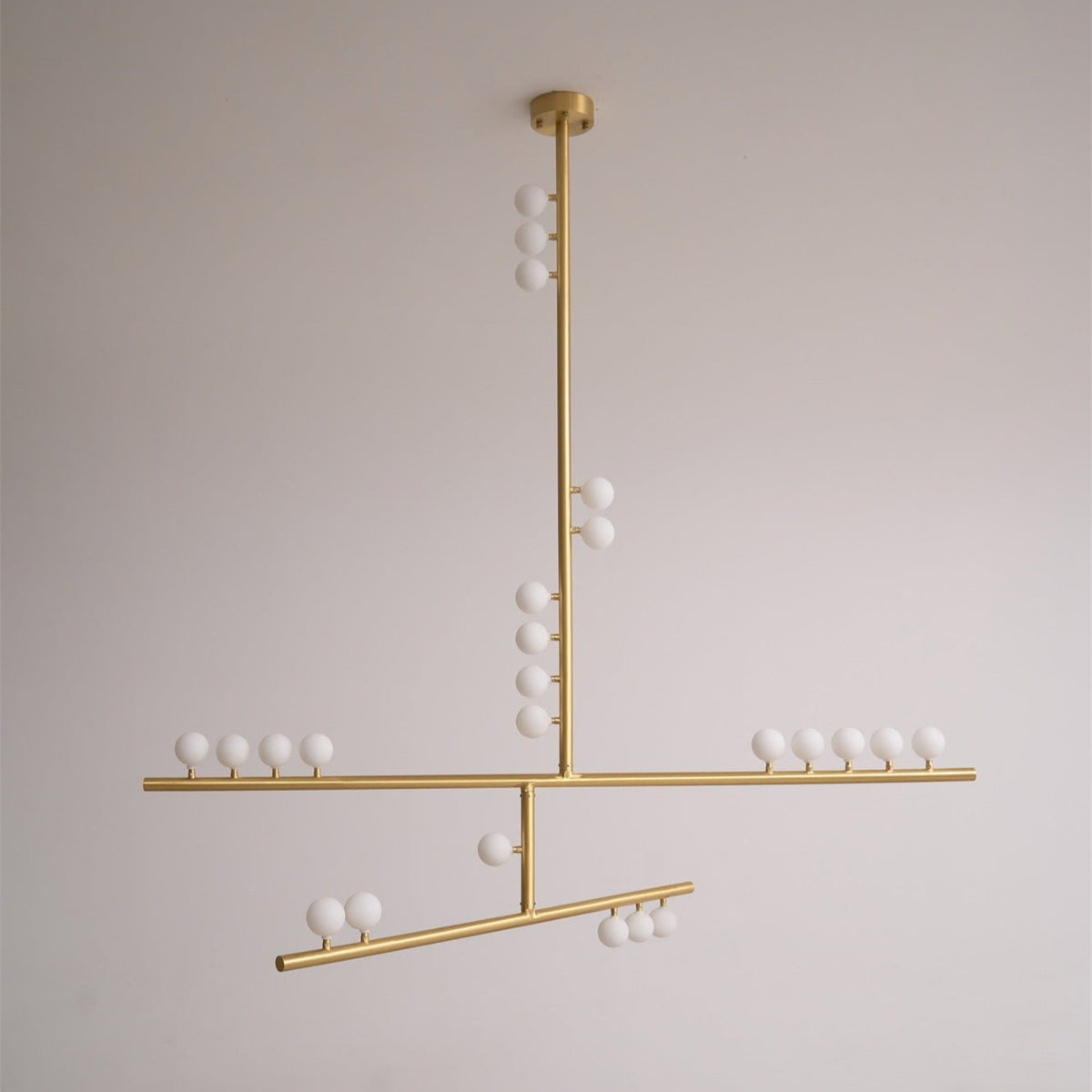 A brass Clérachic pendant with a round ceiling plate and white orbs along its bars, unlit on a pale grey backdrop.