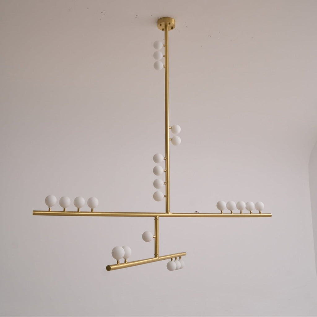 This Clérachic pendant unlit on a pale grey backdrop, with a brass rod, crossed bars and white orbs that look matt.