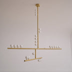 This Clérachic pendant unlit on a pale grey backdrop, with a brass rod, crossed bars and white orbs that look matt.
