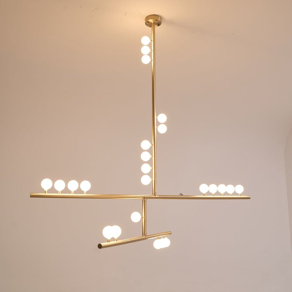 A lit Clérachic pendant with a brass rod and white orbs along two bars, glowing against a warm backdrop.