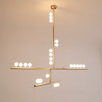 A lit Clérachic pendant with a brass rod and white orbs along two bars, glowing against a warm backdrop.