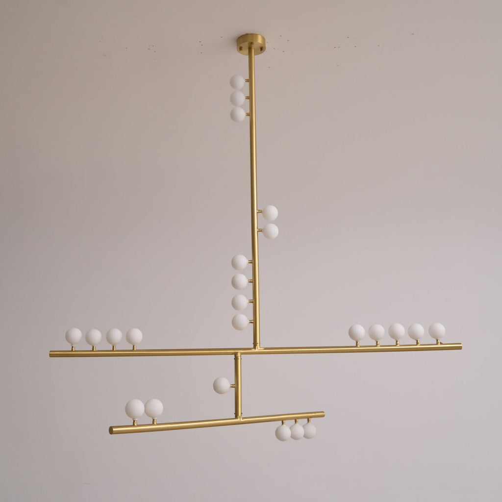 This Clérachic pendant in brass, unlit, hung against a soft grey wall with a clear view of its three bar tiers.