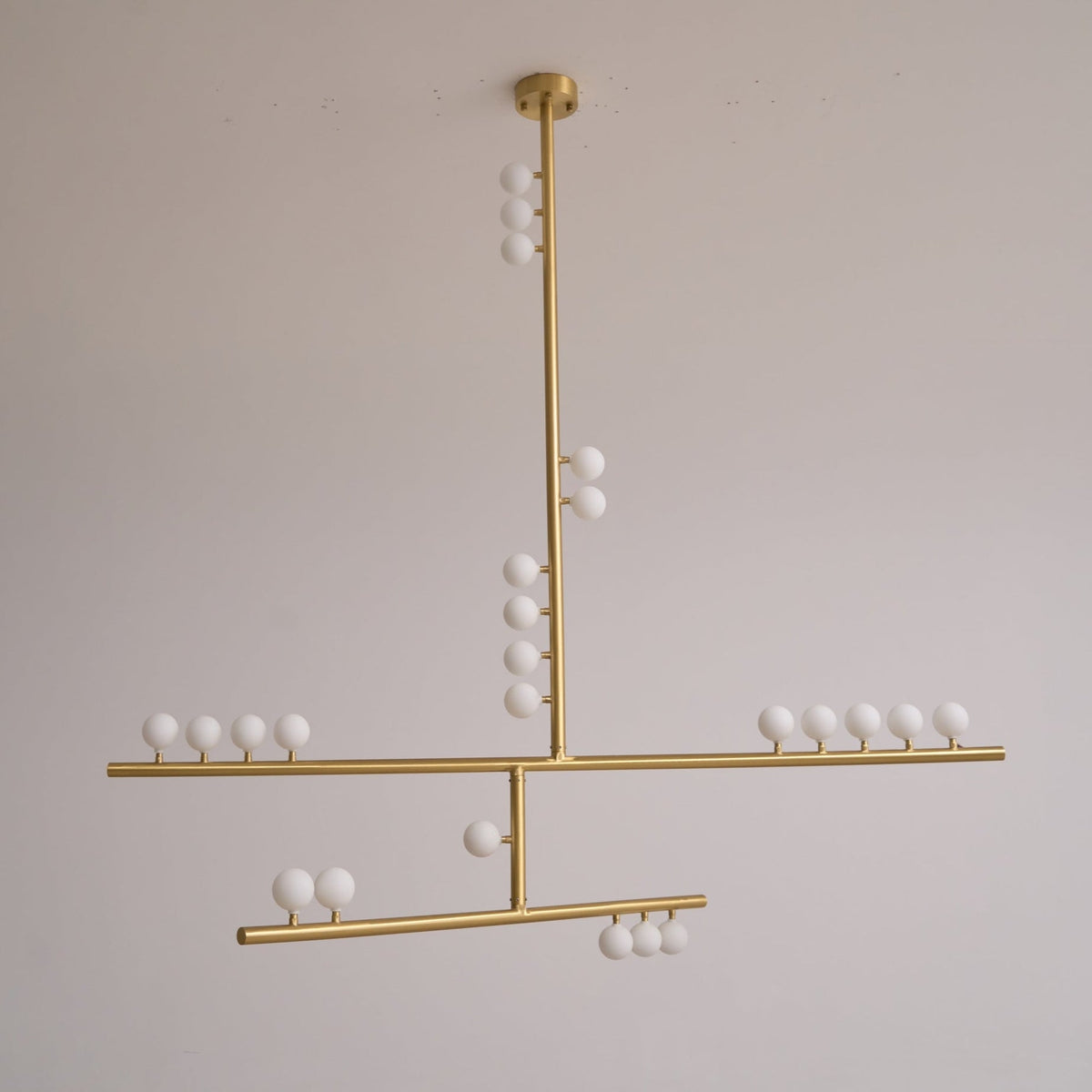 This Clérachic pendant in brass, unlit, hung against a soft grey wall with a clear view of its three bar tiers.