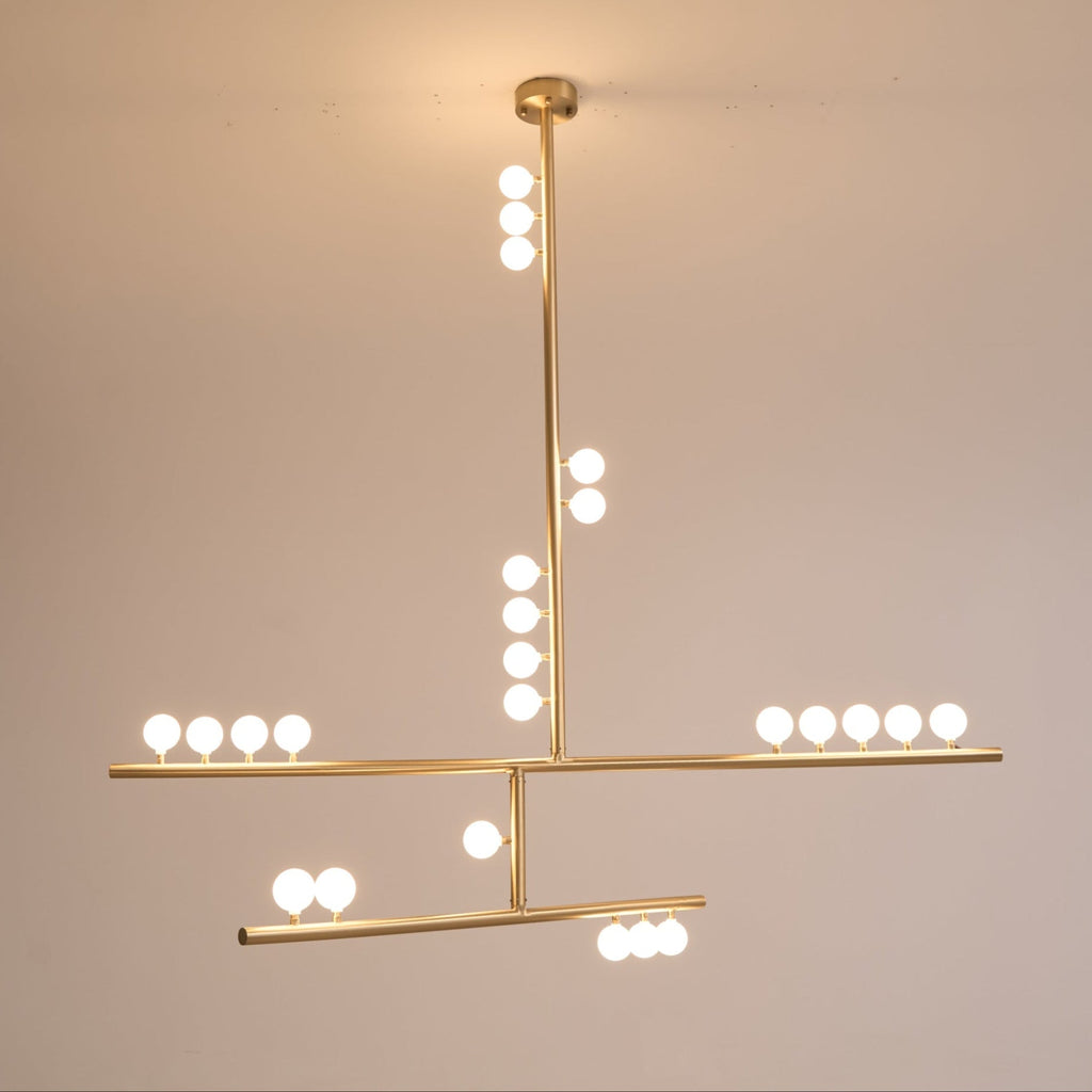 Warm glow from the white orbs on this Clérachic brass pendant, hung against a dusky peach wall.