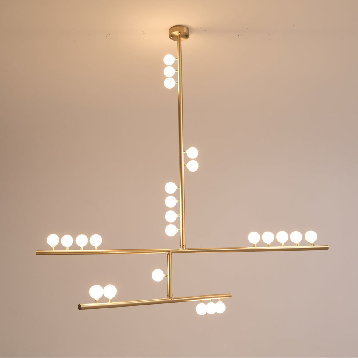 Warm glow from the white orbs on this Clérachic brass pendant, hung against a dusky peach wall.