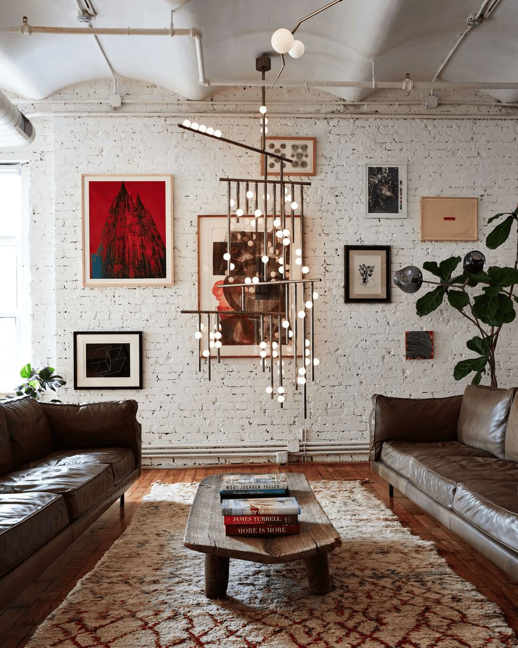 A Clérachic chandelier seen from a distance in a loft with a leather sofa, rug and wooden coffee table beneath it.