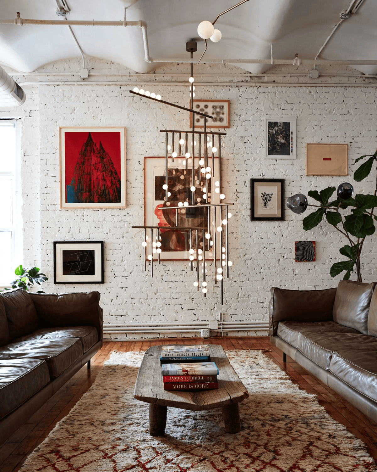 A Clérachic chandelier seen from a distance in a loft with a leather sofa, rug and wooden coffee table beneath it.