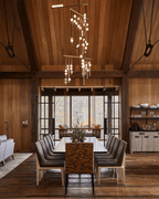 A Clérachic chandelier in a high timber hall, with lit orbs and thin rods hanging over a long dining table.