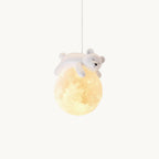 A small white bear lies asleep on a glowing moon-textured globe, this Clérachic pendant light hanging on a plain white backdrop.