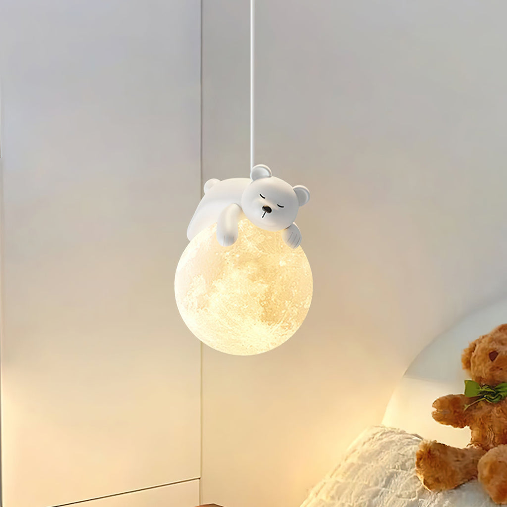 Lit Clérachic pendant with a sleeping bear on a moon-like globe, hanging by a bed with a teddy bear and soft bedding.