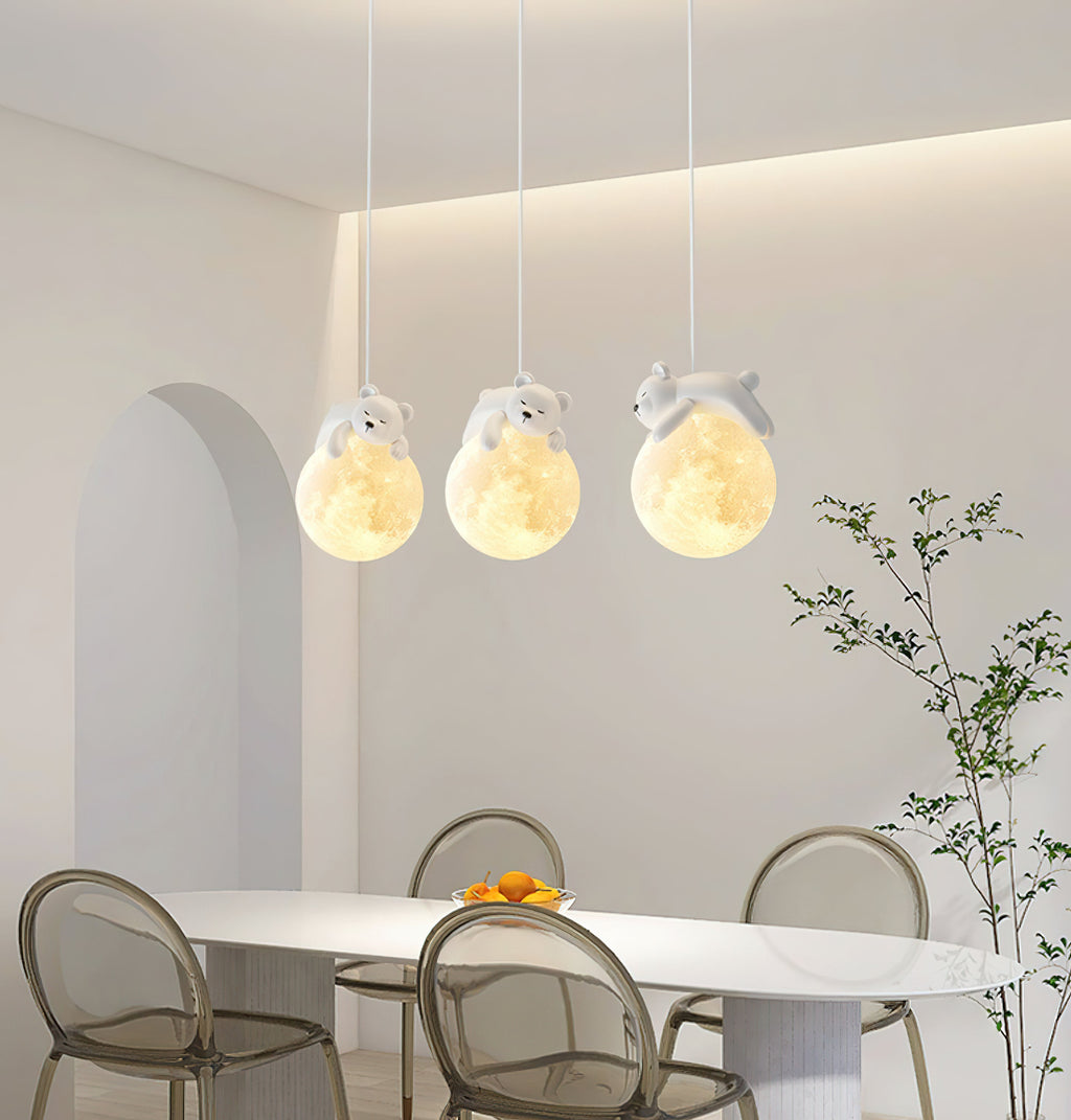 Three Clérachic pendant lights, each with a small sleeping animal on a glowing globe, hang over a white dining table and clear chairs.