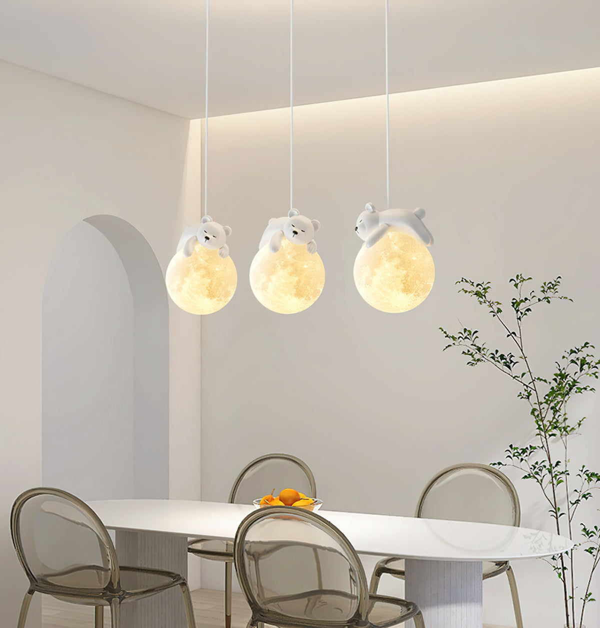 Three Clérachic pendant lights, each with a small sleeping animal on a glowing globe, hang over a white dining table and clear chairs.