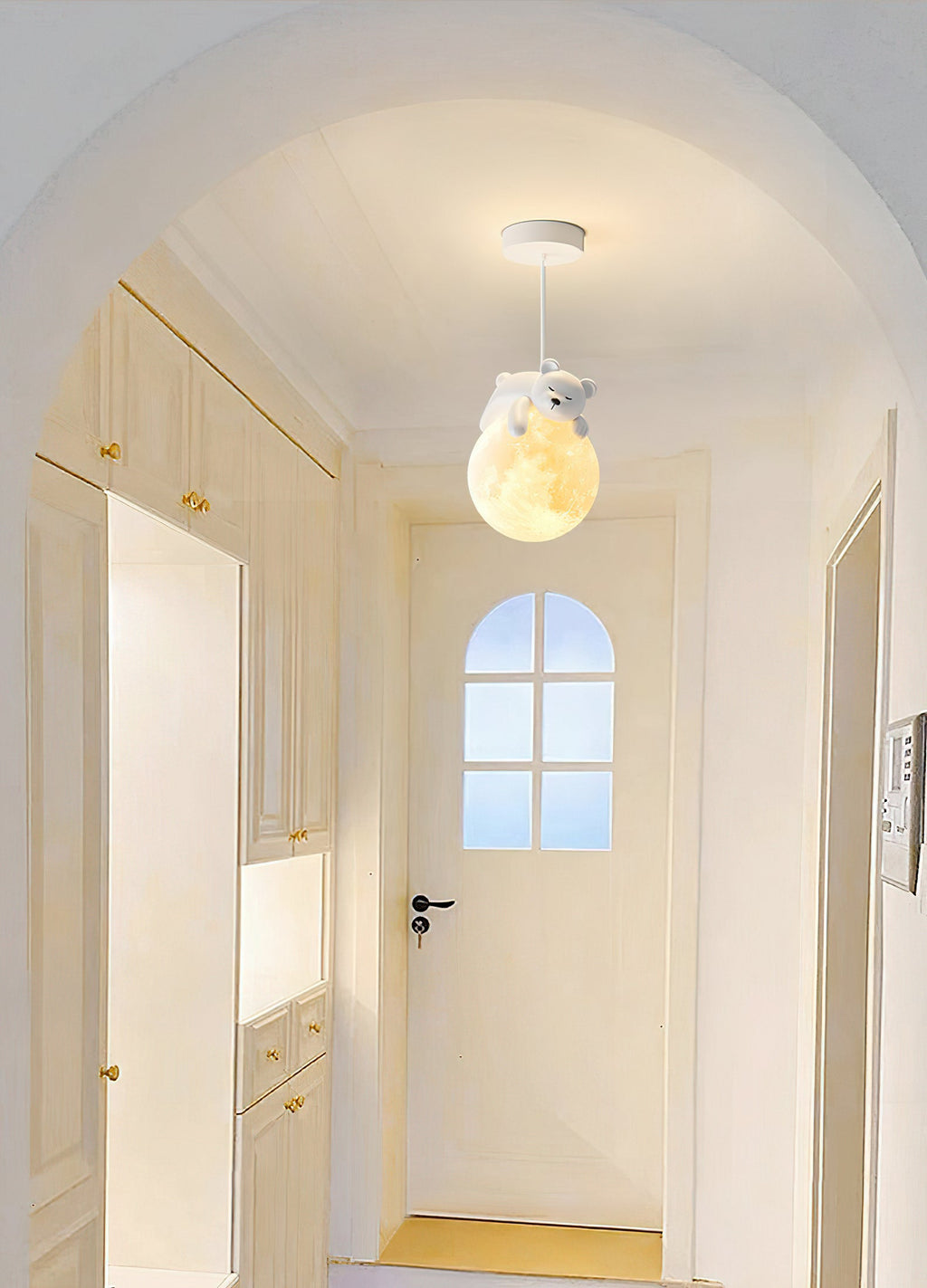 A Clérachic pendant with a bear on a glowing globe hangs from a round ceiling canopy in an arched hallway of pale cabinets.