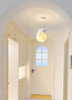 A Clérachic pendant with a bear on a glowing globe hangs from a round ceiling canopy in an arched hallway of pale cabinets.