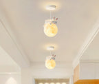 Two Clérachic pendants with rabbit figures on glowing globes hang one behind the other in a narrow, bright corridor.