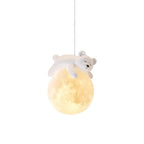 The bear pendant from Clérachic seen on white, with the sleeping figure curled over a softly lit, moon-textured globe.