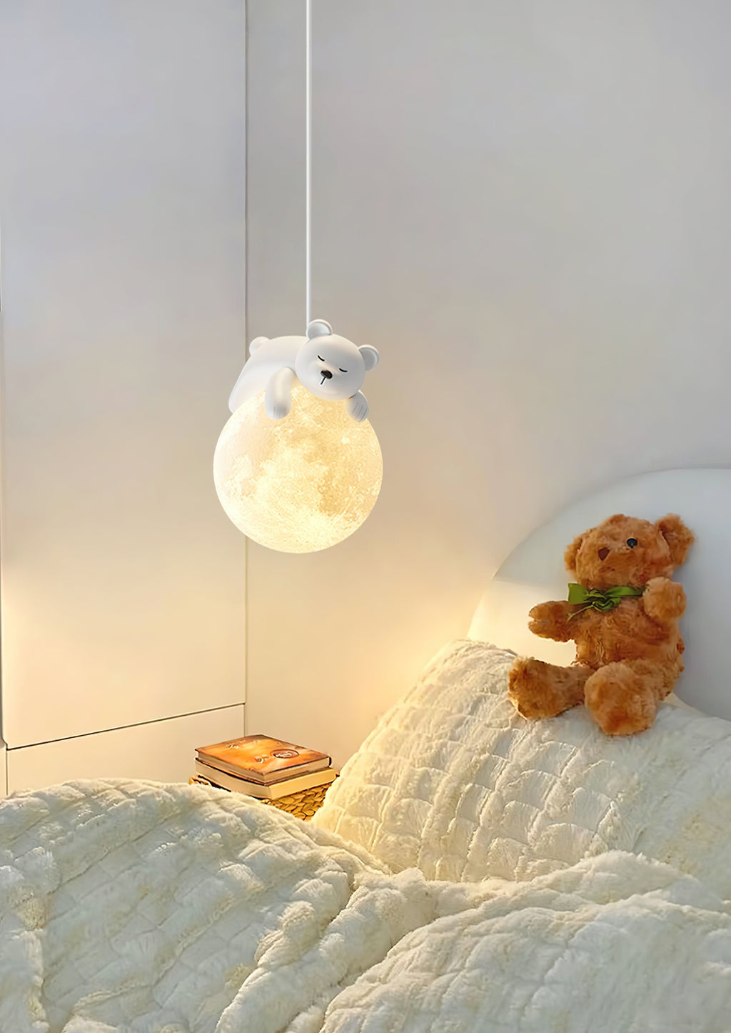A Clérachic pendant with a bear on a moon globe glows above a bed with textured cream bedding and a teddy bear.