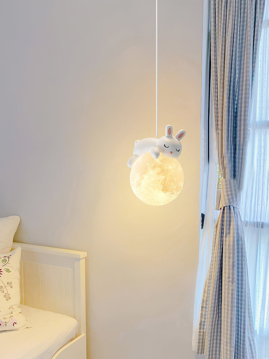 A rabbit pendant from Clérachic glows beside a window with blue checked curtains, with a white daybed at the lower left.