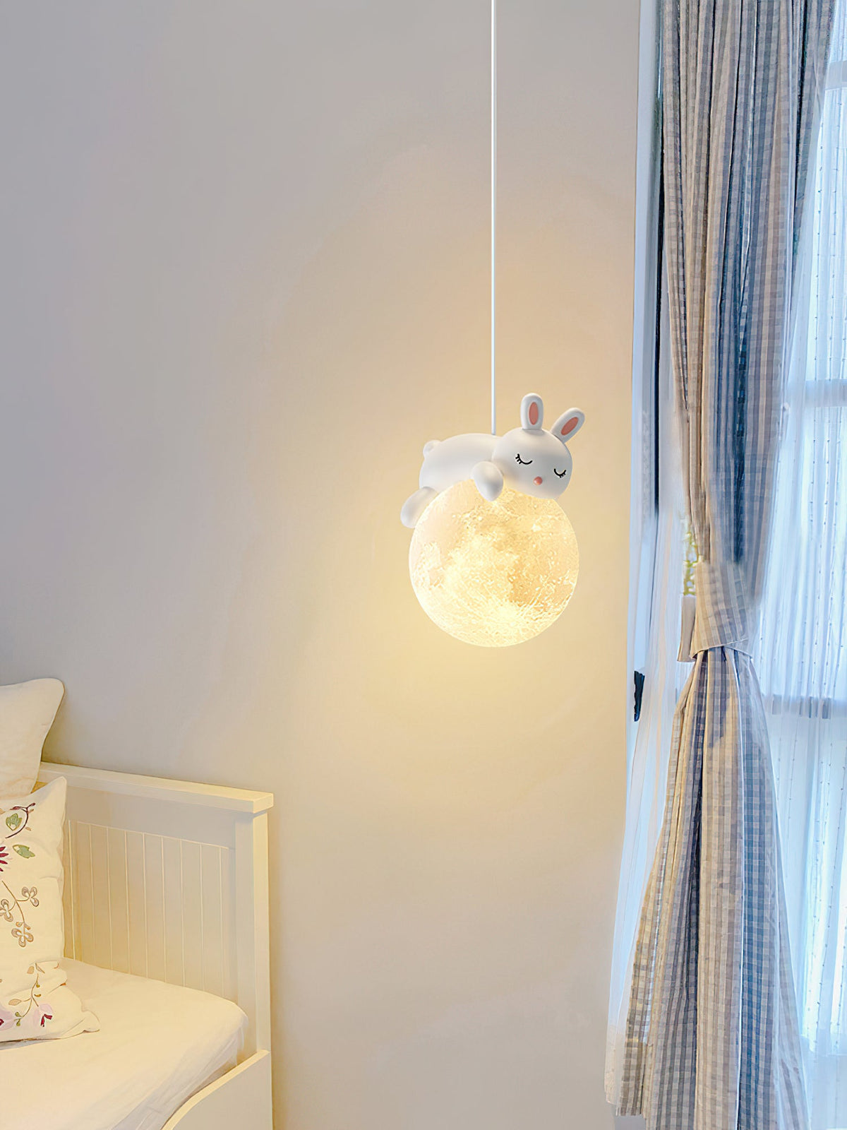 A rabbit pendant from Clérachic glows beside a window with blue checked curtains, with a white daybed at the lower left.