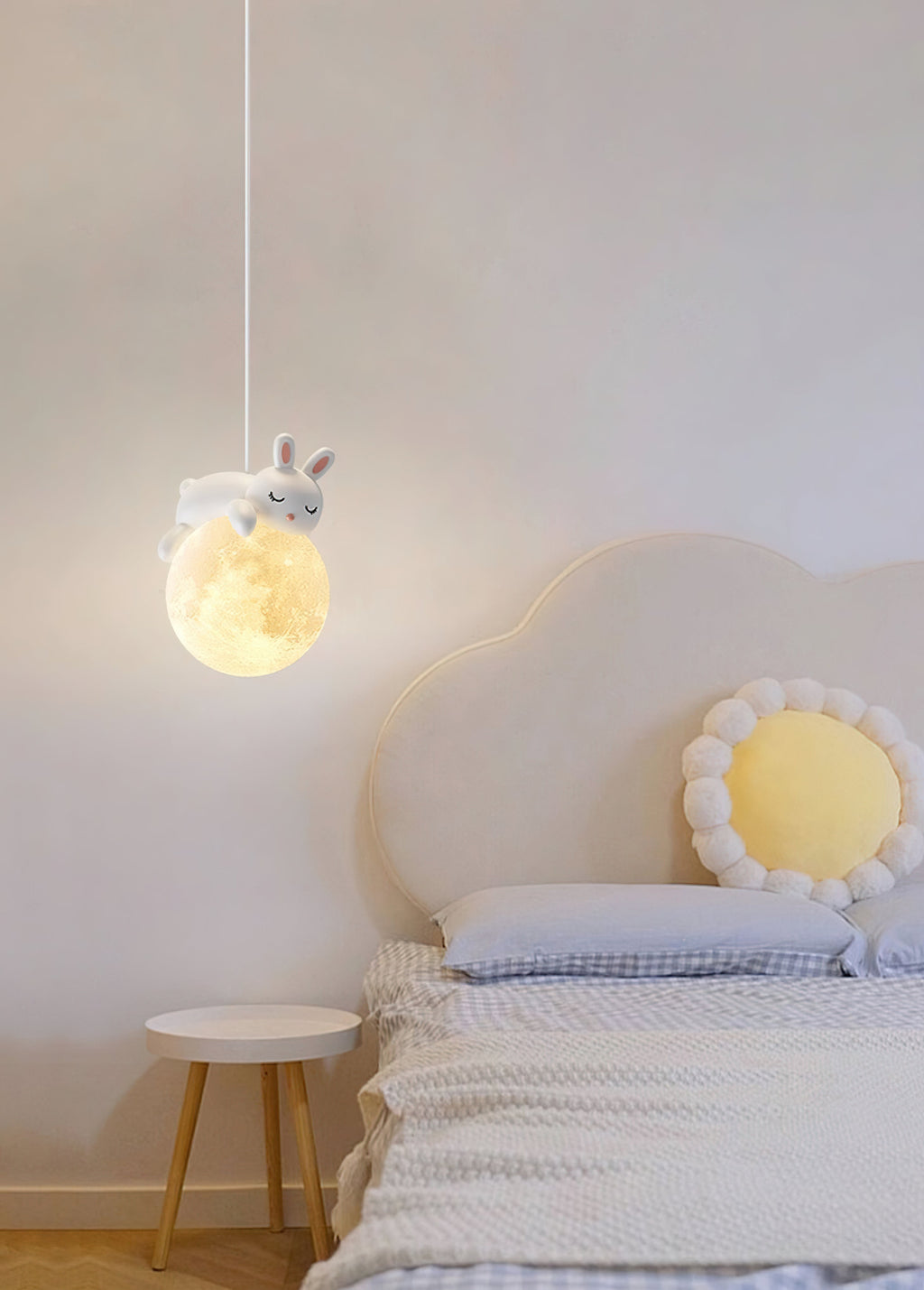 A Clérachic rabbit pendant hangs above a child's bed with a cloud-shaped headboard, a daisy cushion and a small wooden stool.