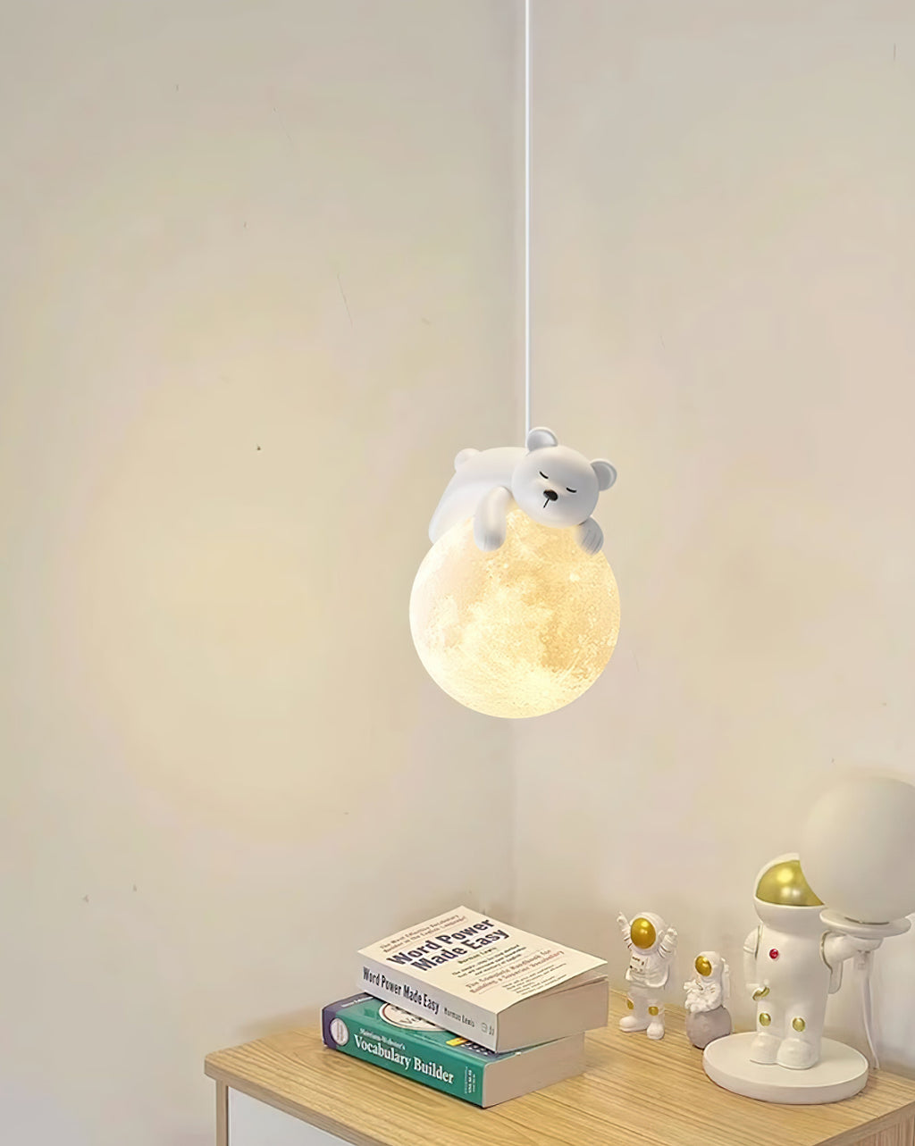 This Clérachic bear pendant glows above a pale wooden bedside table with two books and a small astronaut figure.