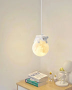 This Clérachic bear pendant glows above a pale wooden bedside table with two books and a small astronaut figure.
