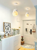 Two Clérachic pendants with small sleeping animals on glowing globes hang in a bright entrance hall above a white sideboard and front door.
