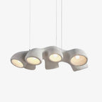 Clérachic pendant on a plain white backdrop, a long textured white form with four rounded openings, each lit by a warm bulb.