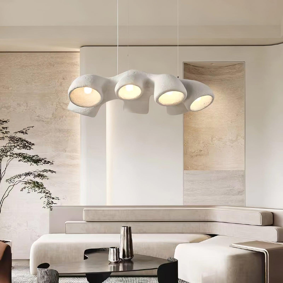 Clérachic pendant hung in a living space with a low cream sofa, a dark glass coffee table and a slim tree beside a soft stone wall.