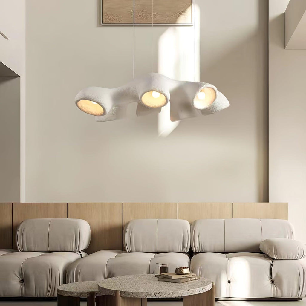 A Clérachic pendant with four lit openings, hanging in sunlight in front of a cream wall and a modular boucle sofa.