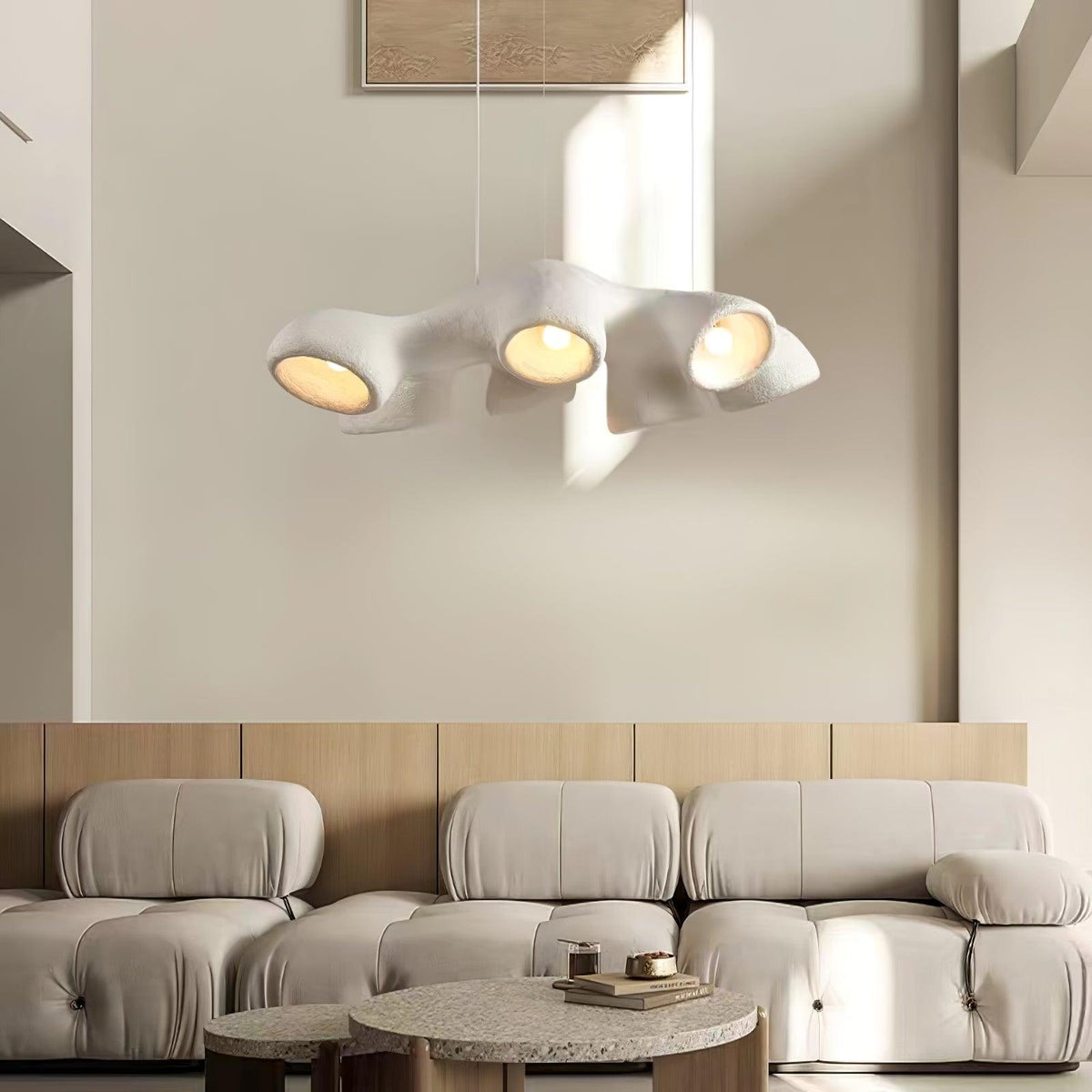 A Clérachic pendant with four lit openings, hanging in sunlight in front of a cream wall and a modular boucle sofa.