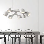 Multi-branch Clérachic pendant in white, each arm ending in a lit opening, above a grey table with black ring-backed chairs.