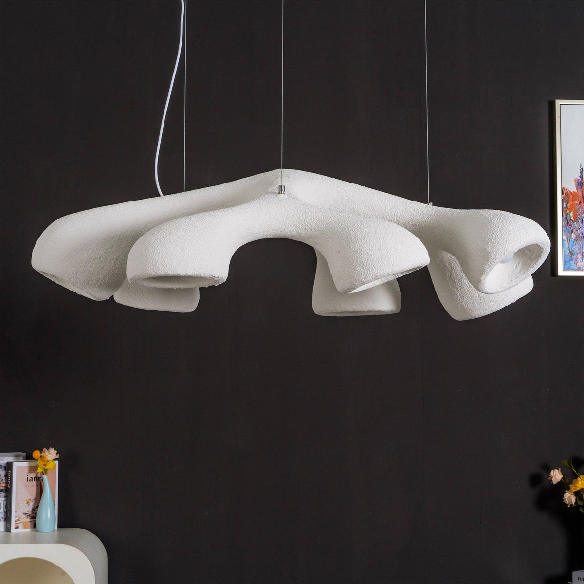 Wide, low angle on a Clérachic pendant against a black wall, showing the rough white surface and the folds between its arms.
