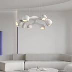Distant view of a Clérachic pendant with branching white arms over a pale sofa and a round low table, in a grey, curved room.