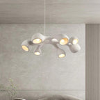 Multi-arm Clérachic pendant hung before a pale wall with vertical ribbing, its lit openings pointing in different directions.