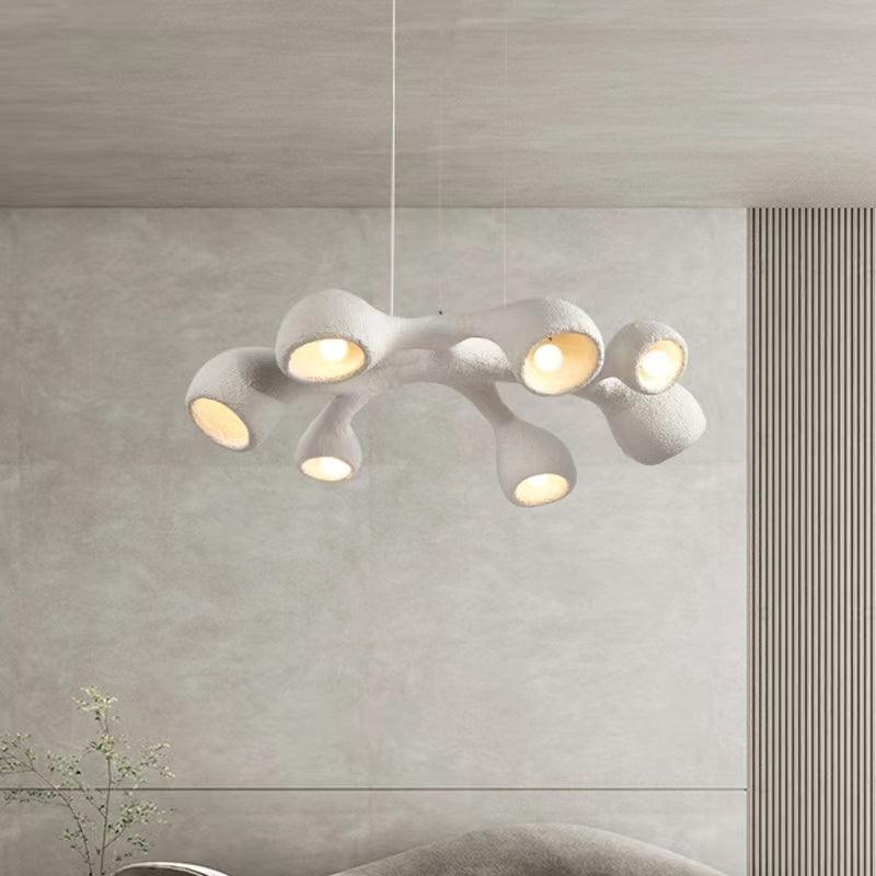 Multi-arm Clérachic pendant hung before a pale wall with vertical ribbing, its lit openings pointing in different directions.