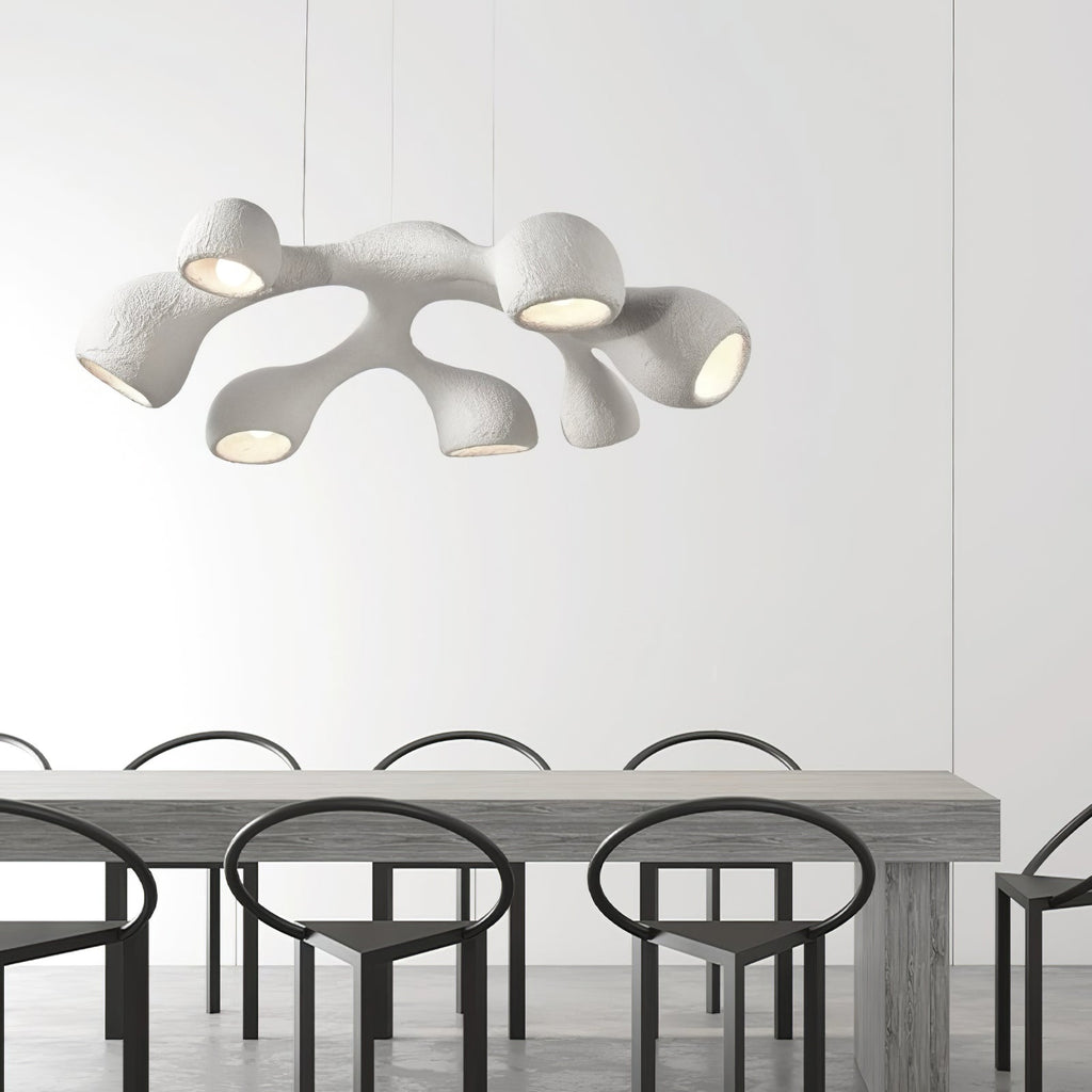 Looking up at a multi-branch Clérachic pendant over a long grey table, with black ring-backed chairs below.