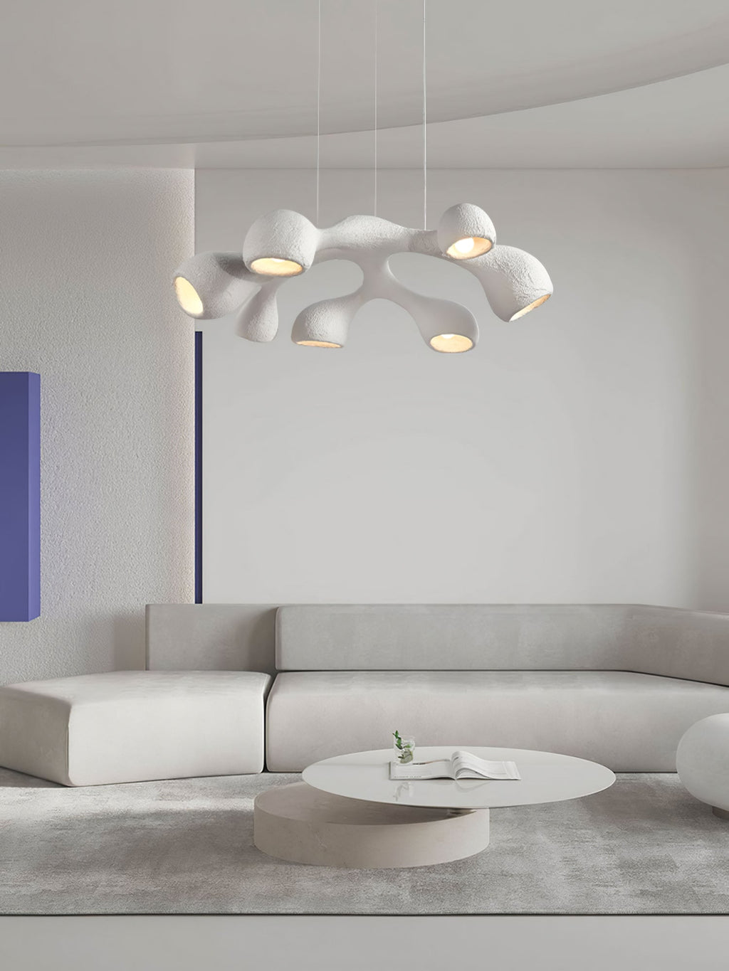 A Clérachic pendant with branching white arms above a pale sectional sofa and a round table, a blue panel at the left.