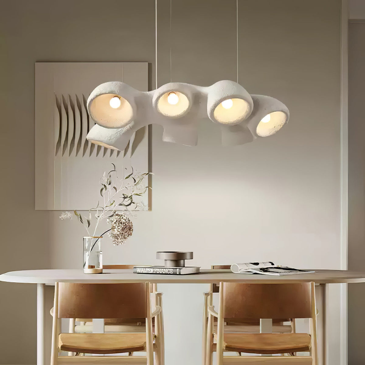 Clérachic pendant with four lit openings over a table set with tan chairs and a dried-branch vase, in a warm neutral room.