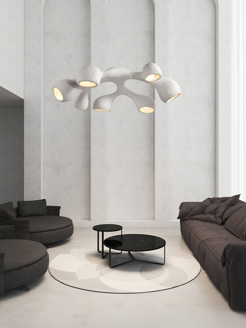 Multi-arm Clérachic pendant in a tall white room with arched wall panels, above a dark sofa pair and black coffee tables.