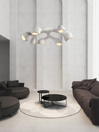 Multi-arm Clérachic pendant in a tall white room with arched wall panels, above a dark sofa pair and black coffee tables.