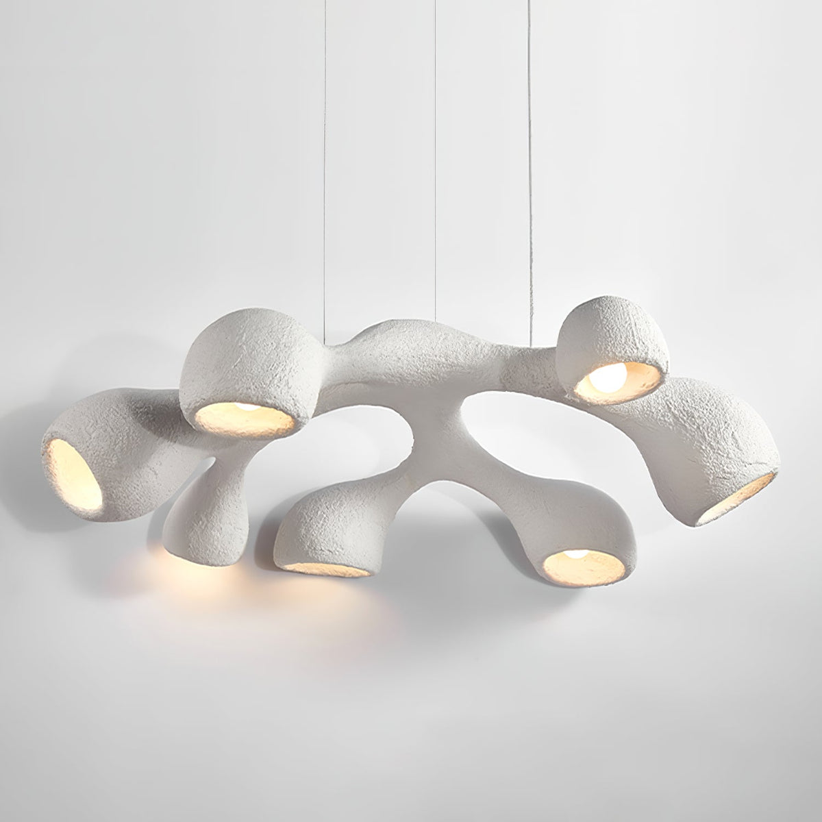 Clérachic pendant seen at an angle, its textured white arms glowing in warm light against a pale grey backdrop.