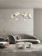 A Clérachic pendant high above a curved grey sofa and a cloud-shaped coffee table, in a room with a ribbed wall panel.