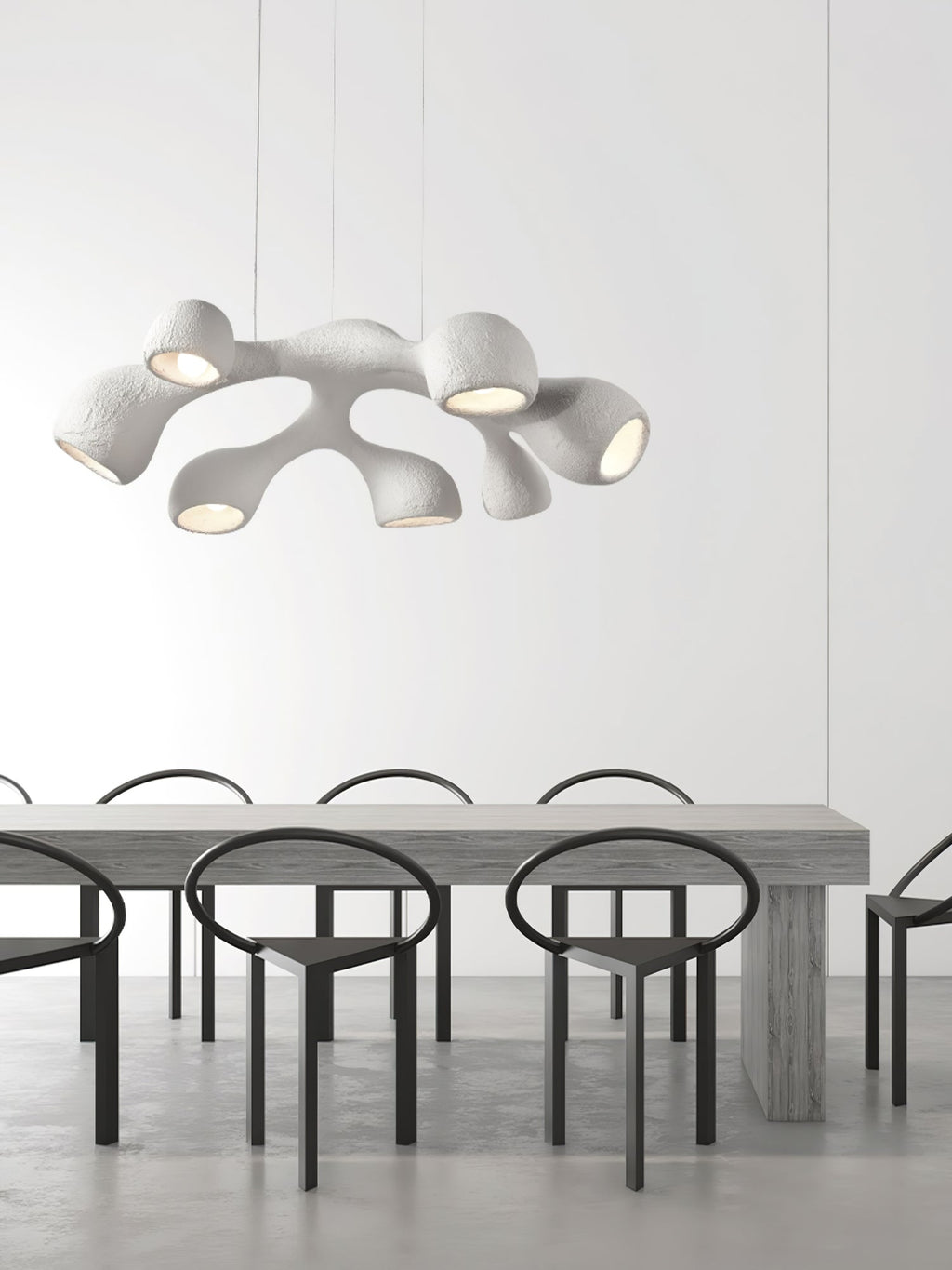 Clérachic pendant hung low above a long grey table with black ring-backed chairs, in a bright minimalist room.