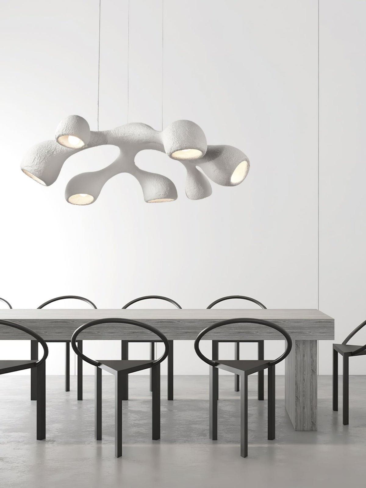 Clérachic pendant hung low above a long grey table with black ring-backed chairs, in a bright minimalist room.