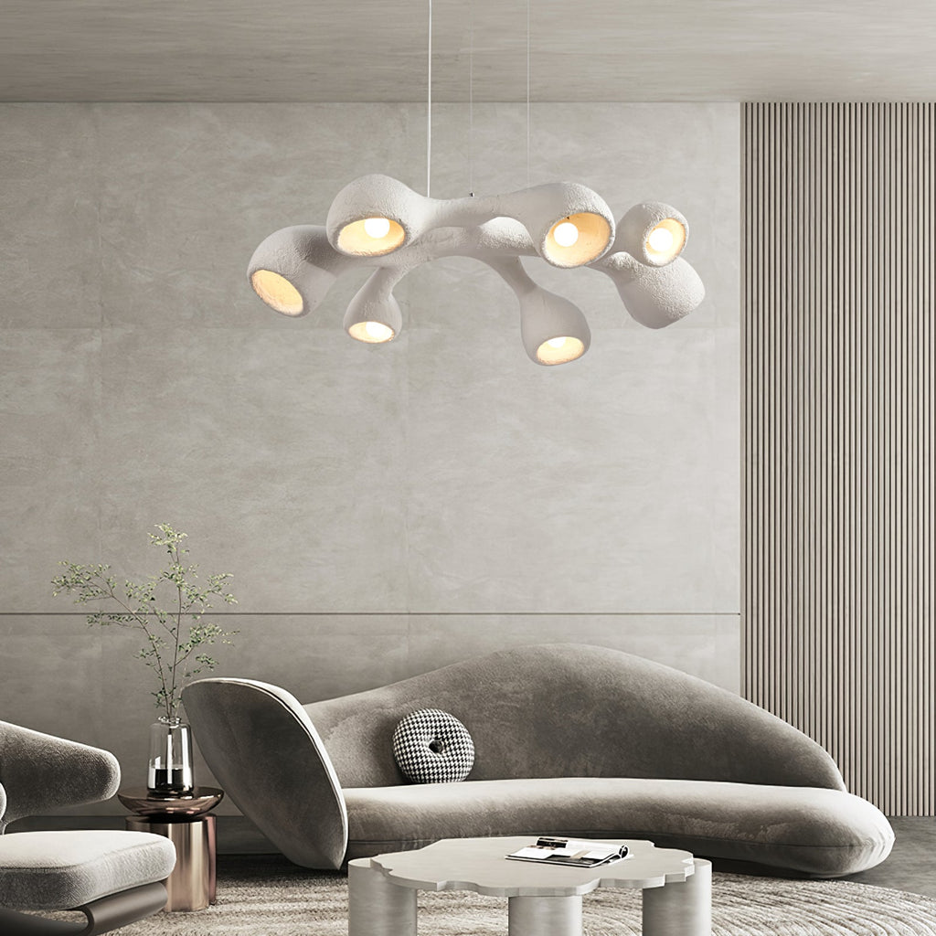 Branching white Clérachic pendant glowing above a curved grey sofa in a room with a ribbed wall and a soft stone-toned panel.