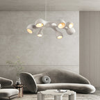 Branching white Clérachic pendant glowing above a curved grey sofa in a room with a ribbed wall and a soft stone-toned panel.