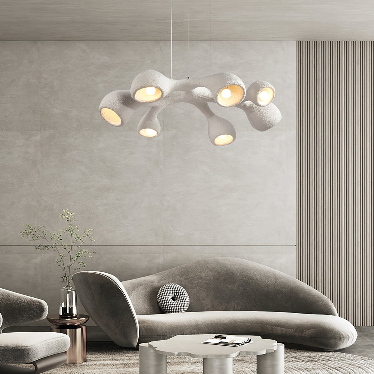 Branching white Clérachic pendant glowing above a curved grey sofa in a room with a ribbed wall and a soft stone-toned panel.